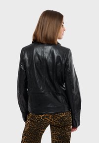 Černá kožená bunda s rovný střih, detailním prošíváním a hladkým povrchem, kombinovaná s hnědými kalhotami s leopardím vzorem.