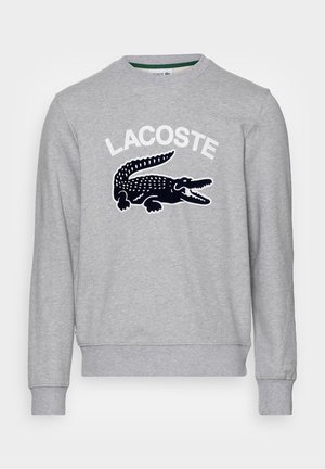 Sweat-shirt gris à manches longues avec col rond, texte blanc "LACOSTE" et grand logo crocodile noir sur la poitrine, poignets et ourlet côtelés.