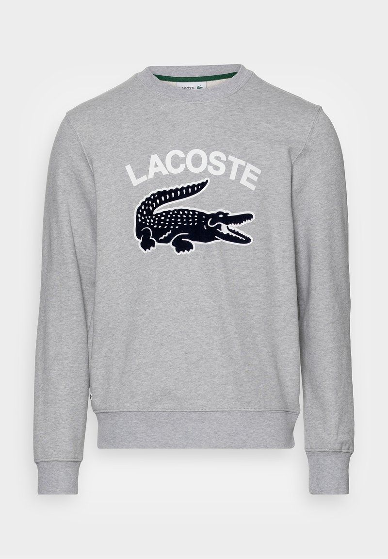 Sweat-shirt gris à manches longues avec col rond, texte blanc "LACOSTE" et grand logo crocodile noir sur la poitrine, poignets et ourlet côtelés.