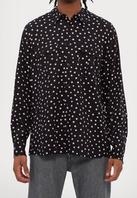Černá košile na knoflíky s potiskem bílých hvězdiček, s límečkem, dvěma předními kapsami a dlouhými rukávy. Hladká tkanina s běžným střihem.