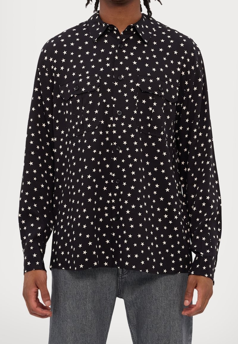 Černá košile na knoflíky s potiskem bílých hvězdiček, s límečkem, dvěma předními kapsami a dlouhými rukávy. Hladká tkanina s běžným střihem.