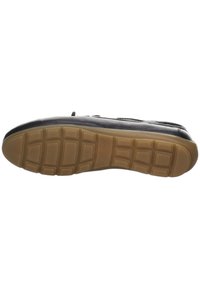 Zapato de cuero negro con suela de goma que presenta un patrón beige texturizado y bloques elevados para tracción. Diseño minimalista sin adornos.