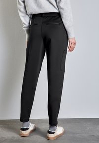 Svarta träningsbyxor med elastisk midja, sidofickor och avsmalnande ben. Bärs med beige och vita sneakers, vilket visar en avslappnad, figursydd design.