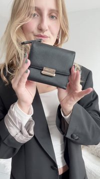 Μαύρο πορτοφόλι με υφή, χρυσές λεπτομέρειες και κλείσιμο με κούμπωμα. Συμπαγής ορθογώνιος σχεδιασμός, μινιμαλιστική αισθητική και καθαρές γραμμές.