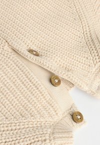 Pull en laine beige avec un motif texturé, comportant trois boutons ronds en bronze et un col doux à côtes.