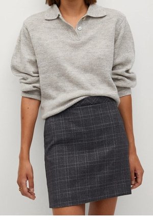Personne portant un pull en maille gris clair à manches longues avec un col et une mini-jupe écossaise gris foncé.