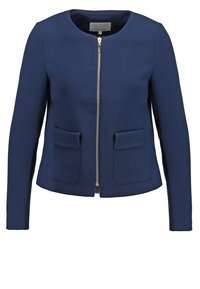 Veste pour femme bleu marine avec encolure ronde, fermeture éclair sur le devant, manches longues et deux poches avant à rabat.