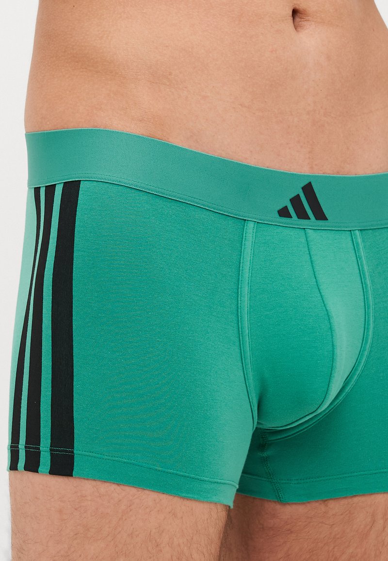 Grüne Boxershorts mit glatter Textur, ausgestattet mit einem schwarzen elastischen Bund und drei schwarzen Streifen an der Seite.