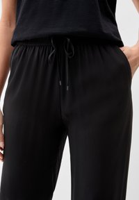 Pantalons noirs à taille élastique avec cordon de serrage, dotés de poches avant et d'une texture lisse et douce.