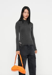 Charcoal geribbelde coltrui met lange mouwen, gecombineerd met donkere cargobroek en een glanzende oranje handtas.
