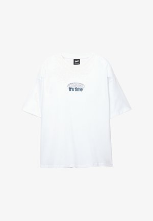 Fehér, rövid ujjú póló, tengerészkék szöveggel: "Itt az idő" és egy hullámos ovális mintával a szöveg felett, középen a mellrészen.