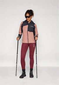 Lekka kurtka w kolorach różowym i granatowym, połączona z dopasowanymi bordowymi legginsami, regulowany kapturem i kijami trekkingowymi.