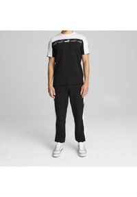 Schwarz-weiße Sportbekleidung mit einem Kurzarmshirt mit Logo und passenden schwarzen Hosen mit weißen Seitenelementen.