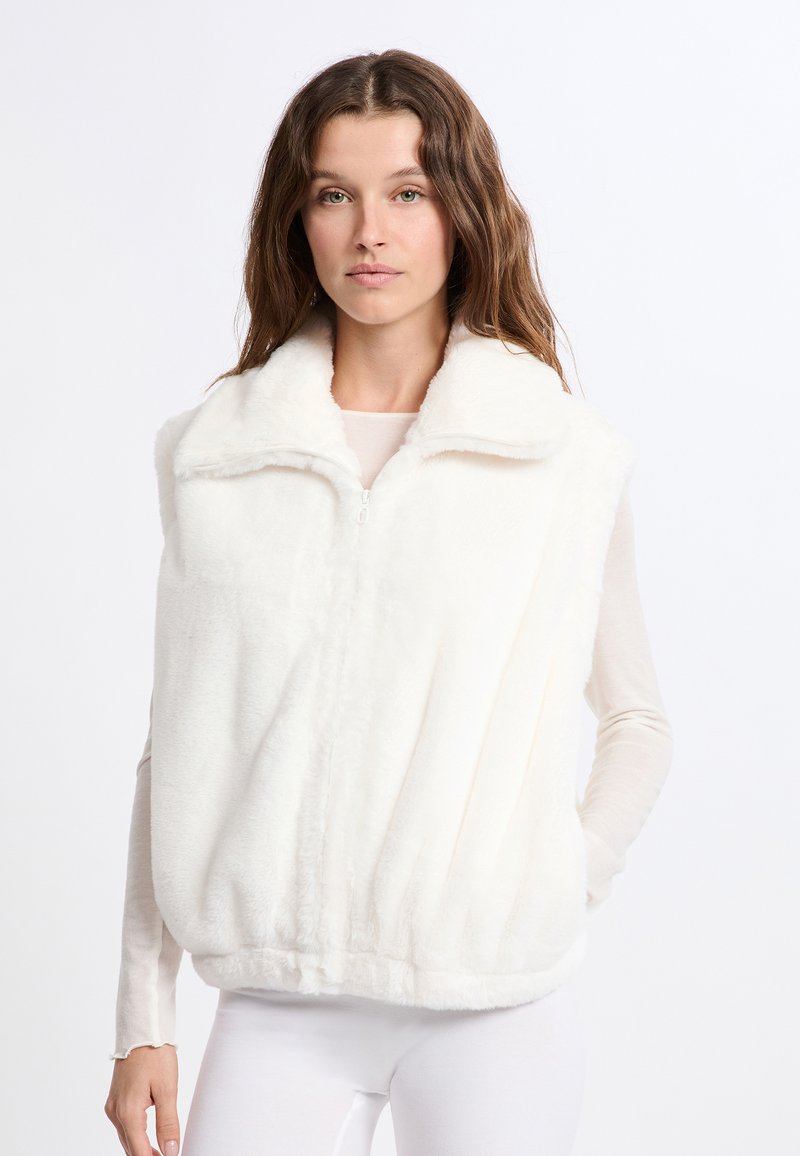 Gilet in finta pelliccia bianca con colletto alto, zip completa e texture morbida. Presenta una vestibilità comoda ed è abbinato a un top leggero.