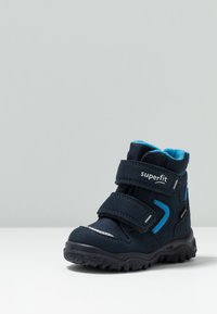 Stivale per bambini blu navy con due cinturini in Velcro, materiali in camoscio e tessuto, fodera a contrasto turchese e suola in gomma nera testurizzata.