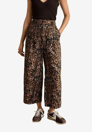 Vida byxor i leopardmönster med en beige och svart färgskala. Har hög midja och sidofickor. Bärs med mörka sneakers.