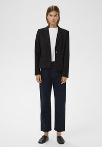 Fekete blézer egy gombbal, alatta fehér póló, sötét farmernadrággal és fekete slip-on cipővel párosítva. Egyszerű, szabott kialakítás.