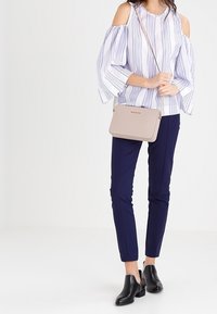 Lätt, off-shoulder blus med vertikala marinblå ränder, i kombination med skräddarsydda marinblå byxor. Kompakt beige axelväska och svarta ankelboots.