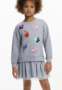 Sweatshirt grigio con toppe di paillettes multicolori (fragola, farfalle, fiori) e testo "dare girl", abbinato a una gonna di tulle grigia shimmer.