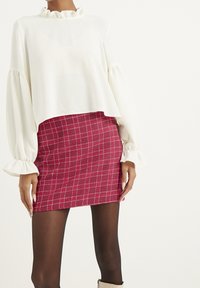 Vit volangblus med puffärmar, kombinerad med en åtsittande mini kjol i röd rutigt mönster, med ett rutig mönster och texturerad tyg.