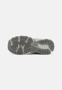 Semelle de chaussure de sport grise avec caoutchouc texturé, présentant des motifs hexagonaux et linéaires pour l'adhérence et la durabilité. Accents de gris clair.