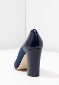 Scarpa con tacco alto blu navy con una punta in pelle verniciata lucida e una tomaia in tessuto testurizzato, dotata di un tacco spesso e solido per garantire stabilità.