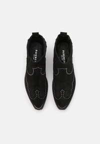 Botines de ante negros con costuras decorativas y tachuelas plateadas. Punta afilada y tirador en la parte trasera para facilitar su puesta. Plantilla texturizada.