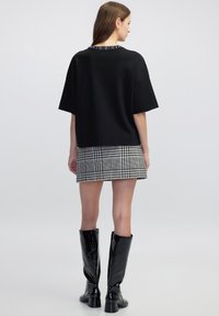 Top negro de gran tamaño con mangas cortas y un dobladillo texturizado, combinado con una falda corta de cuadros en blanco y negro. Botas negras de charol hasta la rodilla.