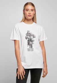Hvit bomulls t-skjorte med svart blomstermotiv og teksten "VENT IKKE TIL DET ER FOR SENT." Korte ermer, rund halsdesign.