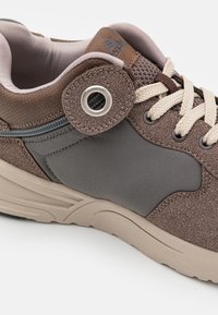 Sapatilha castanha e cinza com um upper texturizado, ilhós redondo, atacadores bege e uma sola almofadada. Apresenta um design suave e curvado.