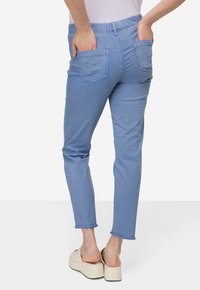 Světlé modré denimové kalhoty s elastickým pasem, dvěma zadními kapsami a slim fit. Lemy jsou mírně roztrhané pro uvolněný vzhled.