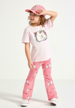 Světlě růžové tričko s motivem kreslené postavičky, doplněné růžovými kalhotami s malými potisky postaviček a srdcí. Bílé tenisky.