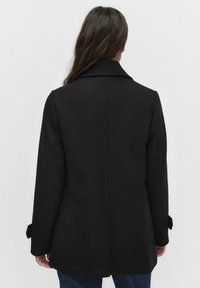 Musta villasekoite takki, jossa on lovettu kaulus, pitkät hihat ja sivutaskut. Suora leikkaus, jossa on hienovaraiset yksityiskohdat hihoissa.