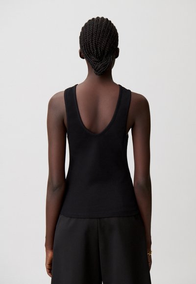 Top negro sin mangas con un escote profundo en forma de U en la espalda, fabricado con una tela lisa y elástica. Lleva pantalones negros de corte holgado.