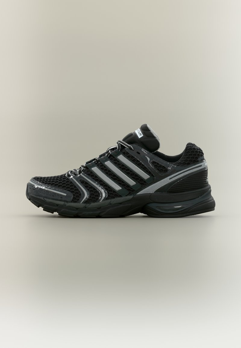 Chaussure de sport noire avec tige en maille, accents argentés, semelle texturée et système de laçage. Comprend un col rembourré et un design élégant et profilé.