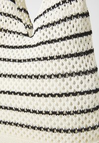 Handwoven cotton bag with a lattice design, featuring alternating white and black horizontal stripes. Textured finish with an open weave.