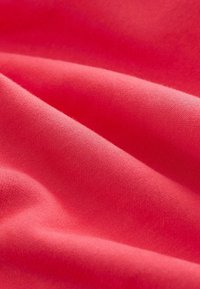 Tissu de couleur corail avec une texture douce et lisse, présentant de légers plis et froissements qui mettent en valeur sa flexibilité et son tombé.