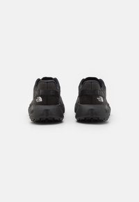 Des chaussures de sport noires présentent un design épuré avec une tige texturée, un talon rembourré et une semelle robuste, portant le logo "The North Face".