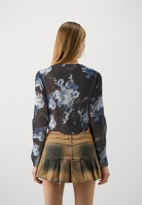 Durchsichtige schwarze Bluse mit blauem Blumenmuster, langen Ärmeln und abgerundetem Saum. Kombiniert mit einem hellbraunen Jeansrock mit ausgestelltem Saum.