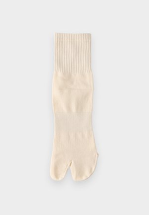 Off-white gebreide tabi-sok met een gespleten teen en geribbelde boorden, plat liggend op een effen lichte achtergrond.