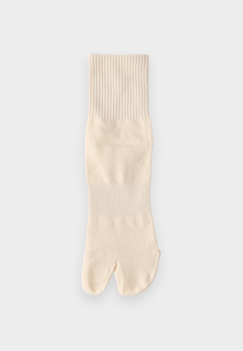 Εκρού πλεκτή κάλτσα tabi με διαχωρισμένο δάχτυλο και ριμπ μανσέτες, απλωμένη επίπεδα σε απλό ανοιχτό φόντο.