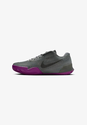 Chaussure de sport Nike avec un dessus texturé gris, un logo noir et une semelle en caoutchouc violette avec un motif en chevrons.
