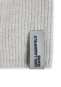 Tessuto a maglia a coste grigio chiaro con una texture liscia, caratterizzato da un'etichetta rettangolare argento con la scritta "KARL LAGERFELD JEANS" stampata in nero.