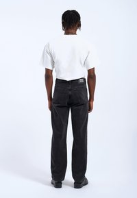 Jeans de denim negro con un corte relajado, que cuentan con un diseño clásico de cinco bolsillos. Combinados con una camiseta blanca de cuello redondo.