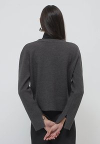 Grau geschnittener Pullover mit langen Ärmeln, weicher Textur, seitlichen Schlitzen und lässiger Passform, von hinten vor einem neutralen Hintergrund gezeigt.