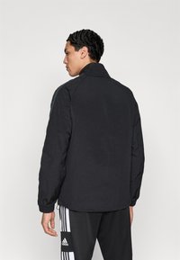 Μαύρο μπουφάν με ανασηκωμένο γιακά, υφή υφάσματος και ραμμένα μανίκια που στενεύουν, με ελαστικά μανίκια και κομψό, μινιμαλιστικό σχέδιο.