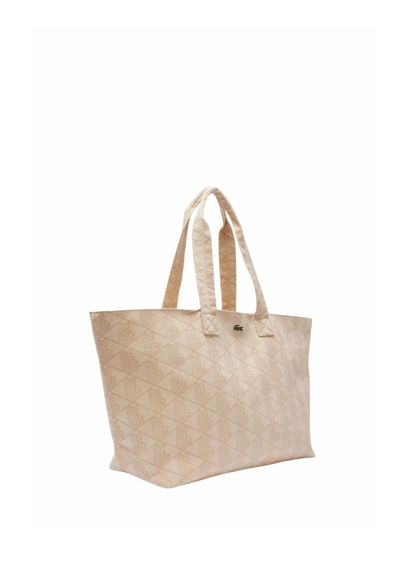 Beige Tragetasche mit geometrischem Muster, zwei Griffen und kleinem grünem Krokodil-Logo vorne.