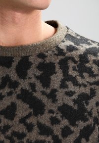 Pullover di lana marrone con un motivo a stampa leopardata nera, collo a coste e texture morbida, vista ravvicinata che mette in evidenza i dettagli del design.