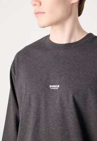 Hanorac lung cu mânecă lungă, de culoare gri închis, cu guler rotund, având un logo alb "Barbour International" pe zona pieptului. Textura moale.
