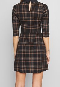 Svart och brunt rutigt klänning med trekvartslång ärm, detalj i ryggen med nyckelhål och en figursydd midja som fläktar ut i en kjol.